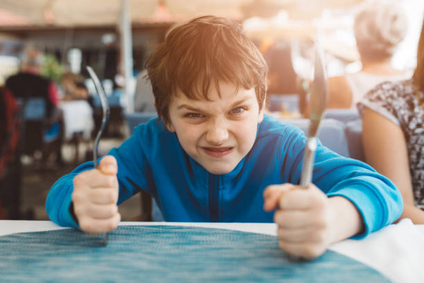 Little boy banging silverware on table ready to eat